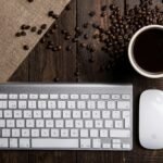 Top view of a coffee cup with keyboard and mouse on a rustic wooden desk.