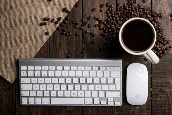 Top view of a coffee cup with keyboard and mouse on a rustic wooden desk.